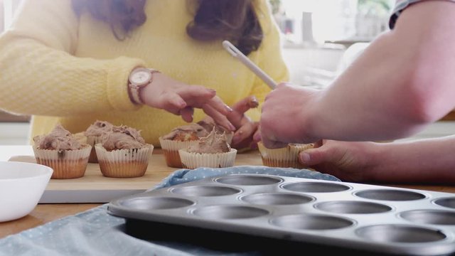 Close Up Of Young Downs Syndrome Couple Decorating Homemade Cupcakes With Icing In Kitchen At Home