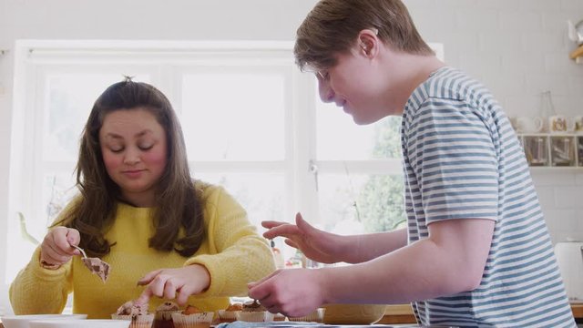 Young Downs Syndrome Couple Decorating Homemade Cupcakes With Icing In Kitchen At Home