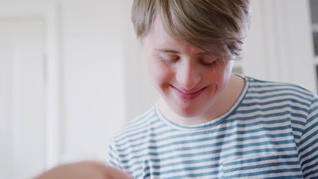 Young Downs Syndrome Man Decorating Homemade Cupcakes With Icing In Kitchen At Home