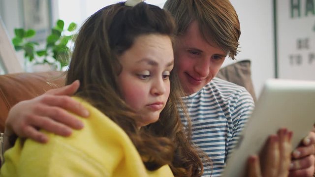 Young Downs Syndrome Couple Sitting On Sofa Watching Digital Tablet At Home