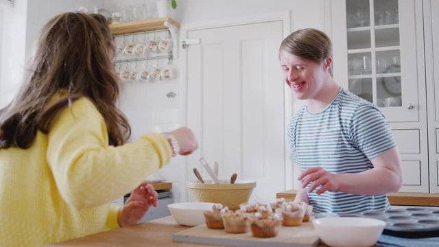 Young Downs Syndrome Couple Decorating Homemade Cupcakes And Dancing In Kitchen At Home
