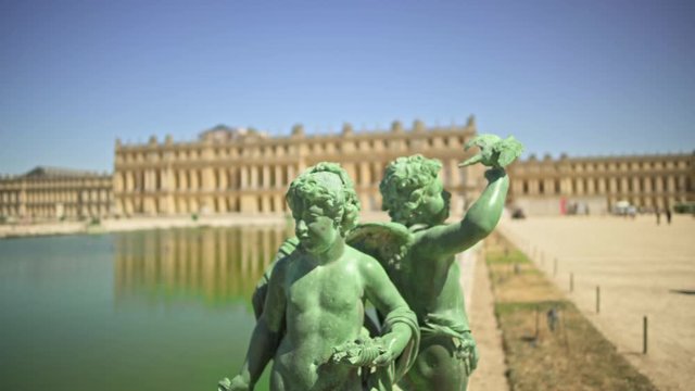 Tilt up shot of green angels on background of blurred lake and Versailles palace in France during spring at daylightf