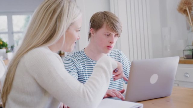 Downs Syndrome Man Sitting With Female Home Tutor Using Laptop For Lesson At Home