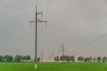 High voltage power lines with electric poles at dusk against the sky