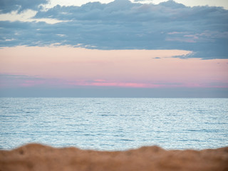 Blue clouds over the light blue sea at the pink sunset with blurred beach