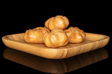 Group of four whole baked golden profiterole on wooden square plate isolated on black glass