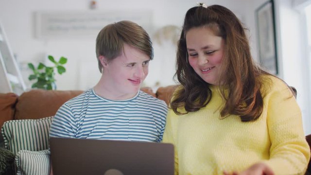Young Downs Syndrome Couple Sitting On Sofa Using Laptop At Home