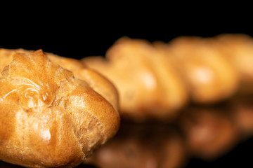 Group of three whole baked golden profiterole one in focus isolated on black glass