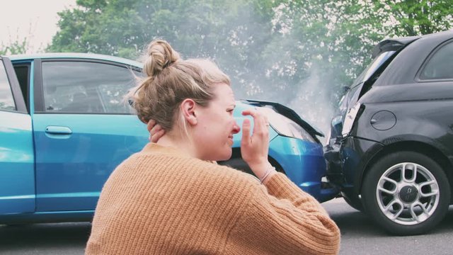Female Motorist With Head In Hands Sitting Next To Vehicles Involved In Car Accident 