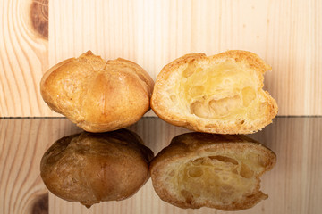 Group of one whole one half of baked golden profiterole on glass with natural wood behind
