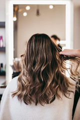 Beautiful brunette woman with long hair at the beauty salon getting a hair blowing. Hair salon styling concept. - obrazy, fototapety, plakaty