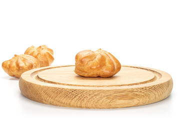 Group of three whole baked golden profiterole one in focus on bamboo plate isolated on white background