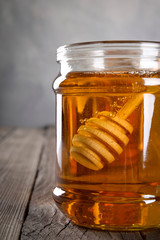 Pouring aromatic honey into jar, closeup. Honey in glass jars and honeycombs wax on wooden background. Wooden stick , instruments