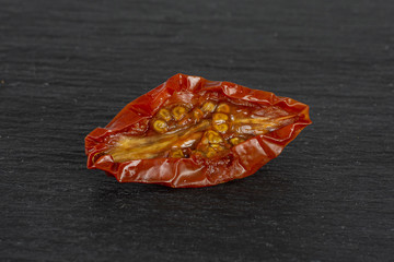 One slice of dry red cherry tomato macro on grey stone