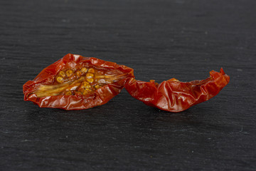 Group of two slices of dry red cherry tomato on grey stone