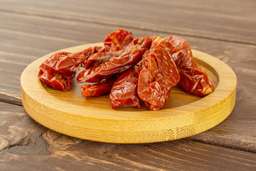 Lot of slices of dry red cherry tomato on bamboo plate on brown wood
