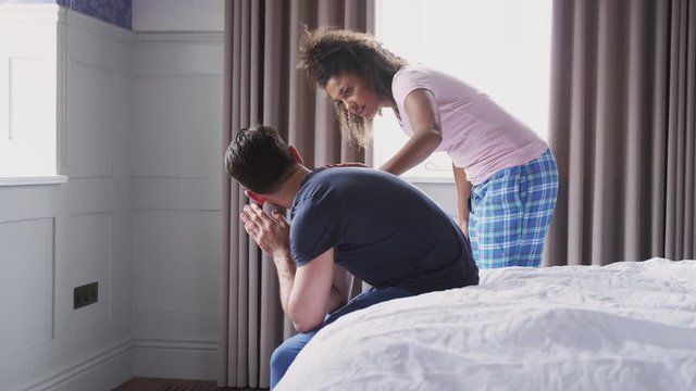 Woman Comforting Man Wearing Pajamas Suffering With Depression Sitting On Bed At Home