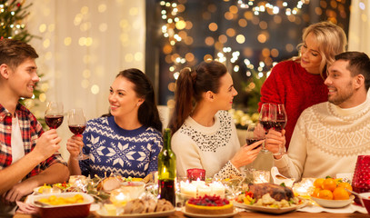 holidays and celebration concept - happy friends having christmas dinner at home, drinking red wine...