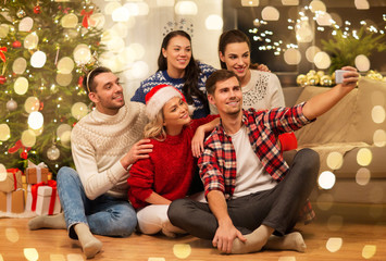 celebration and holidays concept - happy friends with glasses celebrating christmas at home party and taking selfie by smartphone