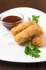Korndog on skewers, breaded and with sauce. On the plate. Close-up.
