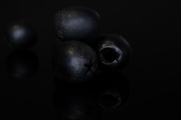 Group of four whole tasty black olive isolated on black glass