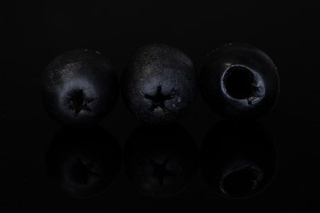 Group of three whole tasty black olive isolated on black glass