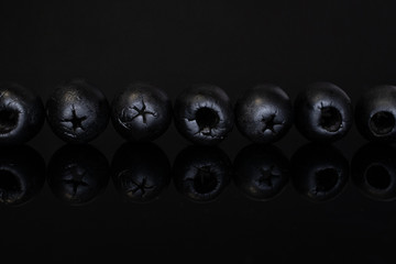 Group of seven whole tasty black olive isolated on black glass