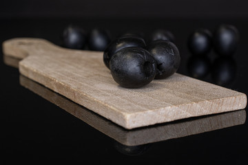 Lot of whole tasty black olive on wooden board isolated on black glass