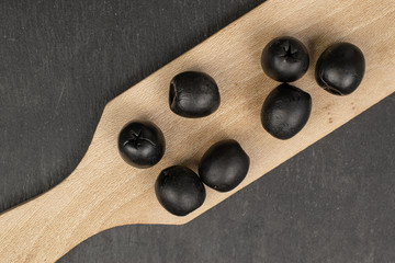 Group of seven whole tasty black olive on wooden board flatlay on grey stone