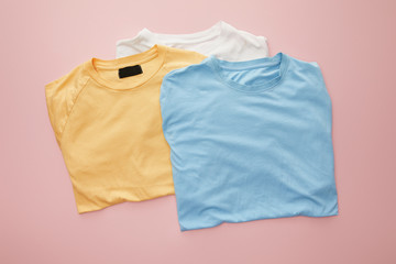 top view of white, yellow and blue folded t-shirts on pink background