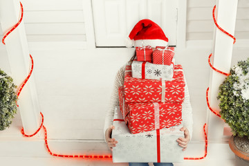 Woman holding a pile of Christmas gift boxes sitting on doorstep outdoors. Xmas gift boxes