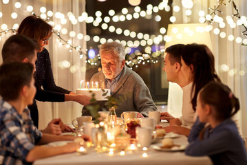 celebration and family concept - happy grandfather blowing candles on birthday cake at dinner party at home