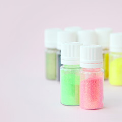 Colorful glitters lies on pastel pink background. Many round jars with multi-colored bright sparkles for nail polish