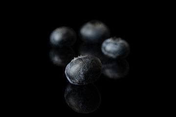 Group of four whole fresh blue blueberry isolated on black glass