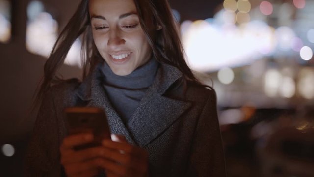 Closeup of prety smiling woman using smartphone walking at night city, slowmotion fullHD stock footage, handheld camera shot