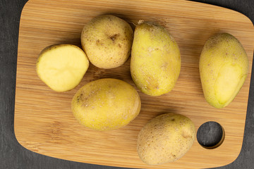 Group of five whole one half of raw brown potato on bamboo cutting board flatlay on grey stone