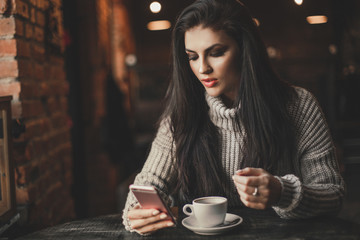 Woman using phone and drinking coffee in a cafe.