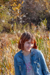 A laughing girl with red hair is standing under the falling fluff. Selective focus on the girl. Autumn forest and bulrushes on a blurred background.