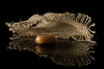 One whole caramel brown candy with jute fabric isolated on black glass