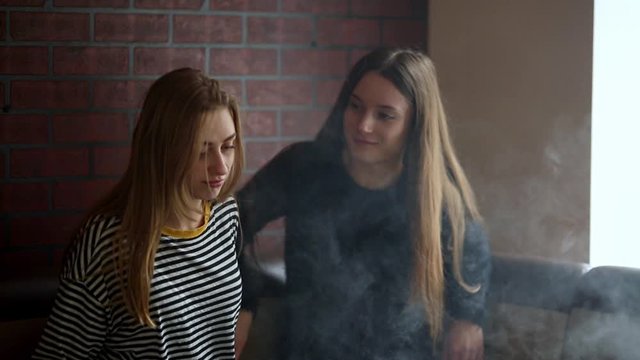 Vape lgbt teenagers. Bisexual lesbian young caucasian teenage girls smoking an electronic cigarette in vape bar. Bad habit that is harmful to health. Young pretty white caucasian teens vaping indoors.