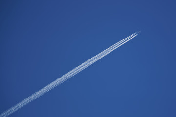 Large four-engine aircraft leaves a trail of four white stripes in the blue sky