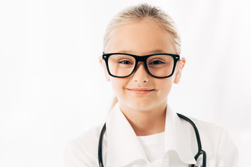 front view of smiling kid in doctor costume and glasses looking at camera isolated on white