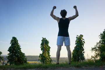 back of sporty man rising his arms as a winner in nature