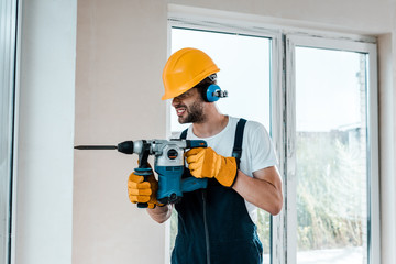 handyman in uniform and yellow gloves using hammer drill