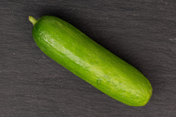 One whole mini green cucumber flatlay on grey stone