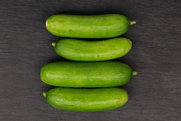 Group of four whole mini green cucumber in row flatlay on grey stone