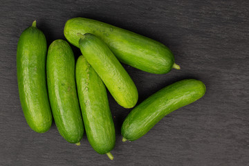 Group of six whole mini green cucumber flatlay on grey stone