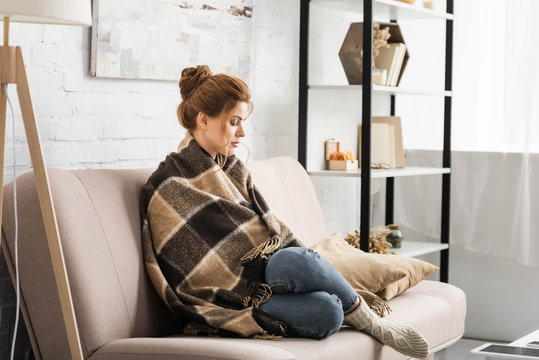 attractive woman with blanket sitting on sofa in apartment
