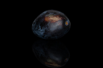 One whole fresh purple plum isolated on black glass