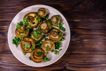 Plate with baked champignons, dill and parsley on a wooden table. Top view